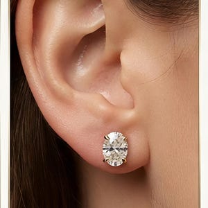 Könnte beinhalten: Ein Ohrstecker mit einem oval geschliffenen, klaren Edelstein in einer vierzinkigen Fassung aus Gelbgold. Der facettierte Stein reflektiert das Licht mit hoher Brillanz und Klarheit und ist mit einem Metallstift sicher am Ohrläppchen befestigt.