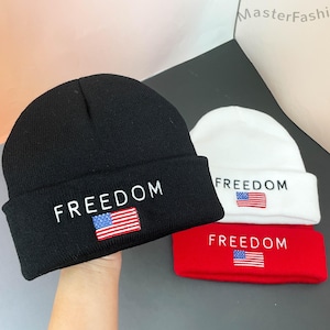 May include: Three knitted beanies in black, white, and red. Each beanie features the word "FREEDOM" embroidered in white, and a small American flag. The beanies are made of a soft material.
