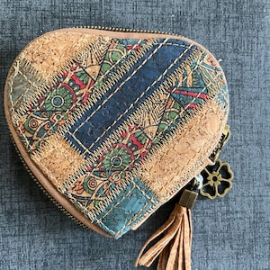 May include: Heart-shaped cork wallet with a patchwork design. The wallet features a zipper closure, a tassel, and a decorative charm. The patchwork includes blue, green, red, and tan patterned fabric.
