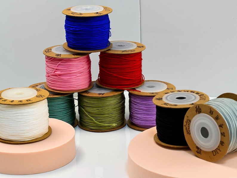 Puede incluir: Una colecci&oacute;n de coloridas bobinas de cord&oacute;n el&aacute;stico en varios colores, incluyendo azul, rosa, rojo, verde, morado, negro y blanco. Las bobinas est&aacute;n apiladas y dispuestas sobre una superficie blanca.