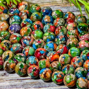May include: A collection of round, multi-colored gemstone beads. The beads are a mix of green, blue, red, brown, and white. The beads are all about 1 cm in diameter.