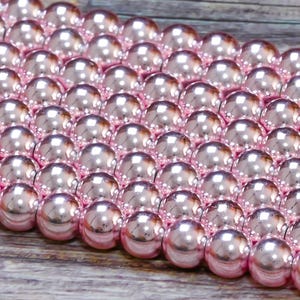 May include: A close-up of a strand of pink pearl beads. The beads are round and have a glossy finish.