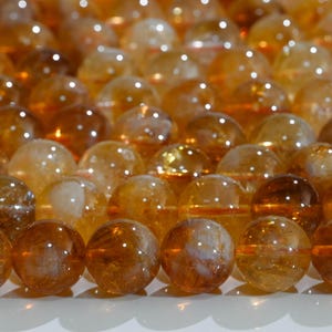 May include: Close-up of a collection of polished, translucent citrine gemstone spheres. The spheres vary in shades of amber and gold, with internal inclusions visible. The arrangement suggests a focus on natural crystals and gemstones.