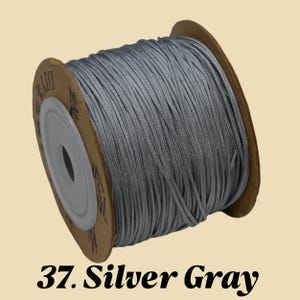 Puede incluir: Un carrete de cord&oacute;n gris plateado. El cord&oacute;n est&aacute; enrollado alrededor de un n&uacute;cleo de cart&oacute;n. El texto "37. Silver Gray" est&aacute; impreso en la parte inferior de la imagen.
