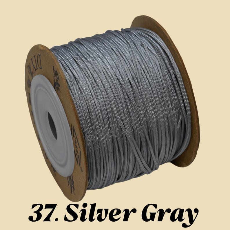 Puede incluir: Un carrete de cord&oacute;n gris plateado. El cord&oacute;n est&aacute; enrollado alrededor de un n&uacute;cleo de cart&oacute;n. El texto "37. Silver Gray" est&aacute; impreso en la parte inferior de la imagen.