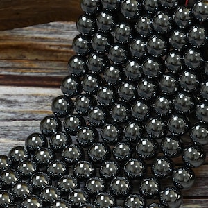 May include: A strand of black hematite beads, each bead is round and smooth, with a high polish. The beads are arranged in a cascading pattern, creating a visually appealing display.