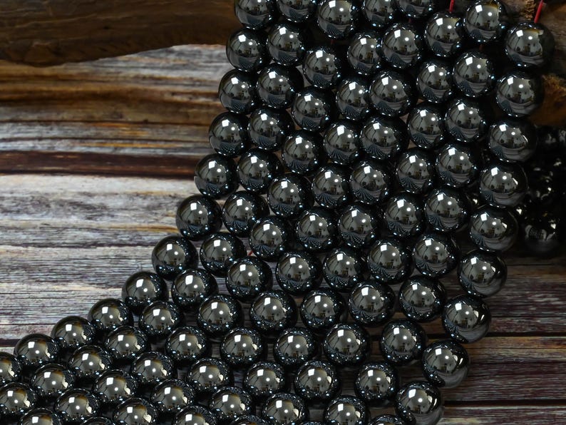 May include: A strand of black hematite beads, each bead is round and smooth, with a high polish. The beads are arranged in a cascading pattern, creating a visually appealing display.