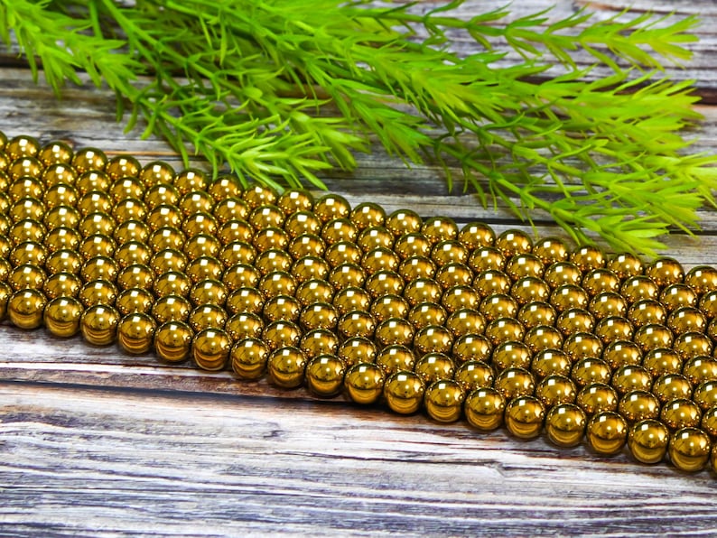 K&ouml;nnte beinhalten: Nahaufnahme einer Reihe gl&auml;nzender goldener Perlen. Die Perlen sind in einem Gittermuster angeordnet und alle gleich gro&szlig;. Die Perlen liegen auf einer Holzoberfl&auml;che.