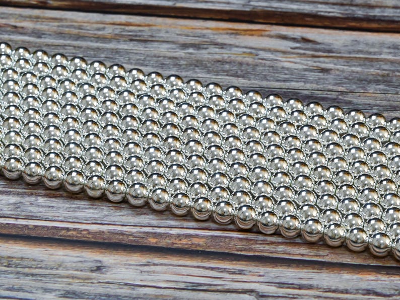 Puede incluir: Primer plano de una gran cantidad de bolas de metal de color plateado dispuestas en filas. Las bolas son lisas y brillantes, y est&aacute;n dispuestas en un patr&oacute;n escalonado.