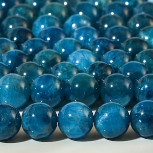 May include: Close-up of a collection of polished, round, blue-green gemstone beads. The beads have a glossy finish and vary in shades of teal and turquoise. The beads are arranged closely together, creating a textured surface.