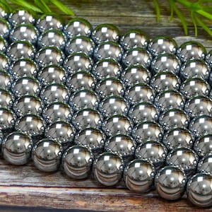 May include: A close-up of a large quantity of round, silver-colored beads. The beads are arranged in a staggered pattern, creating a visual texture.