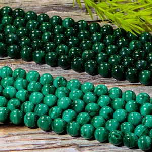 May include: Close-up of several strands of polished, round, dark green malachite beads. The beads are strung together, showcasing their natural patterns and glossy finish. The beads are a vibrant green color.