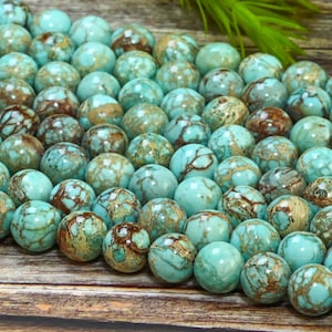 Puede incluir: Una hebra de cuentas redondas de color azul turquesa y marrón marmolado. Las cuentas tienen un aspecto moteado y manchado.