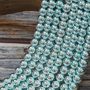 May include: A strand of light blue iridescent glass beads. The beads are round and have a smooth, shiny finish.