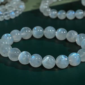 May include: A stretch bracelet composed of smooth, round, translucent white moonstone beads. Each bead exhibits a subtle, iridescent blue sheen that catches the light, creating a glowing effect across the circular arrangement of the polished gemstone spheres.