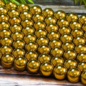K&ouml;nnte beinhalten: Nahaufnahme einer gro&szlig;en Menge gl&auml;nzender goldener Perlen. Die Perlen sind rund und glatt und in einem Muster angeordnet.