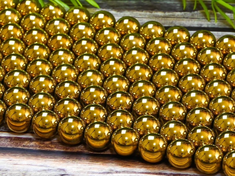 K&ouml;nnte beinhalten: Nahaufnahme einer gro&szlig;en Menge gl&auml;nzender goldener Perlen. Die Perlen sind rund und glatt und in einem Muster angeordnet.