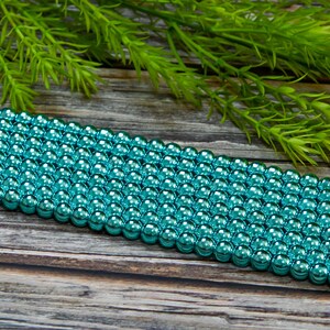 May include: A strand of turquoise metallic round beads. The beads are arranged in rows and have a shiny, reflective finish.