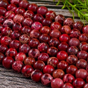 May include: A strand of red and white marbled jasper beads. The beads are round and have a speckled appearance.