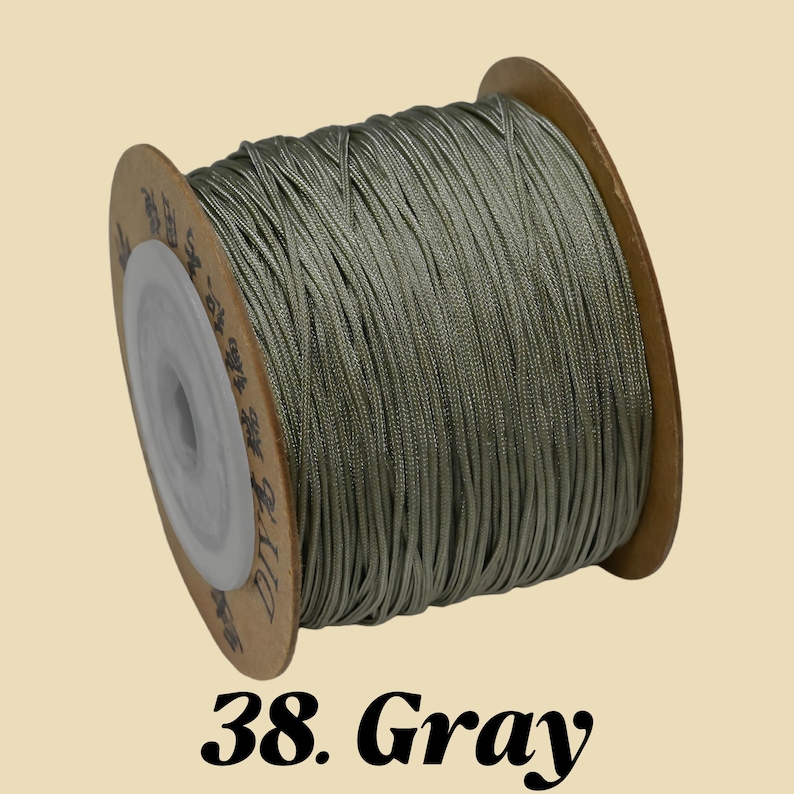 Puede incluir: Un carrete de cord&oacute;n gris. El cord&oacute;n est&aacute; enrollado alrededor de un carrete de cart&oacute;n con un n&uacute;cleo de pl&aacute;stico blanco. El texto "38. Gray" est&aacute; impreso en negro en la parte inferior de la imagen. El cord&oacute;n parece estar hecho de un material liso y brillante.
