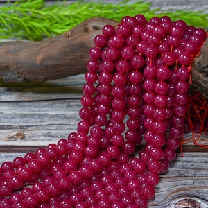Peut inclure: Plusieurs rang&eacute;es de perles rondes de pierres pr&eacute;cieuses rouge fonc&eacute;. Les perles sont enfil&eacute;es sur un fil rouge, cr&eacute;ant un aspect fluide et textur&eacute;. Le fond comprend du bois et de la verdure. Id&eacute;al pour la cr&eacute;ation de bijoux.