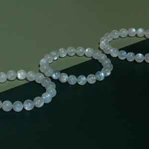 Puede incluir: Tres pulseras circulares hechas de cuentas redondas, lisas y transl&uacute;cidas con un brillo p&aacute;lido e iridiscente. Cada pulsera est&aacute; construida con una sola hebra de piedras pulidas de color claro que muestran sutiles reflejos de luz azul.