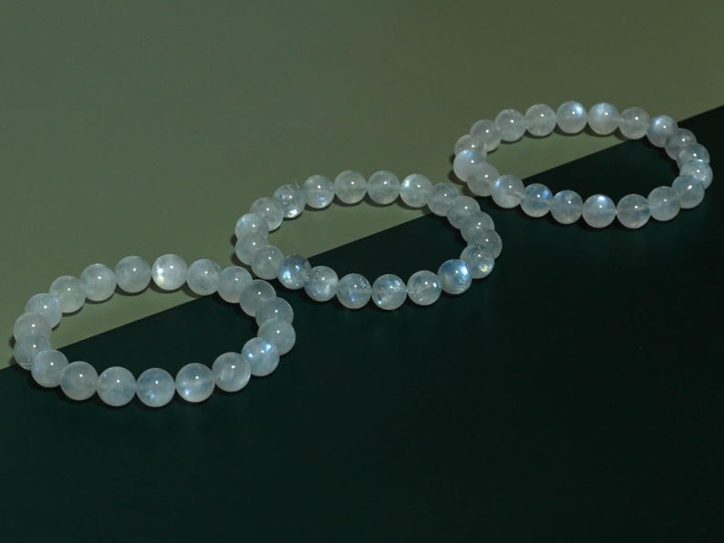 Puede incluir: Tres pulseras circulares hechas de cuentas redondas, lisas y transl&uacute;cidas con un brillo p&aacute;lido e iridiscente. Cada pulsera est&aacute; construida con una sola hebra de piedras pulidas de color claro que muestran sutiles reflejos de luz azul.