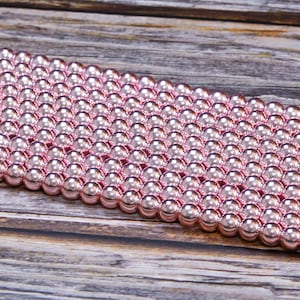 Op de afbeelding: Een streng roze metalen kralen. De kralen zijn rond en hebben een glanzende afwerking.