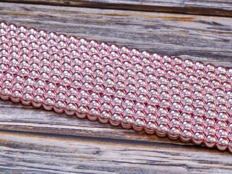 Op de afbeelding: Een streng roze metalen kralen. De kralen zijn rond en hebben een glanzende afwerking.