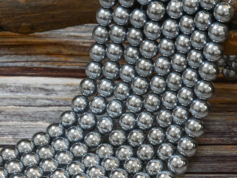 May include: A strand of silver-toned round beads, each bead is smooth and reflective. The beads are arranged in a cascading pattern, creating a visual texture.