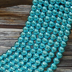 May include: A strand of turquoise blue glass beads with a metallic sheen. The beads are round and smooth, and they are arranged in a cascading pattern.