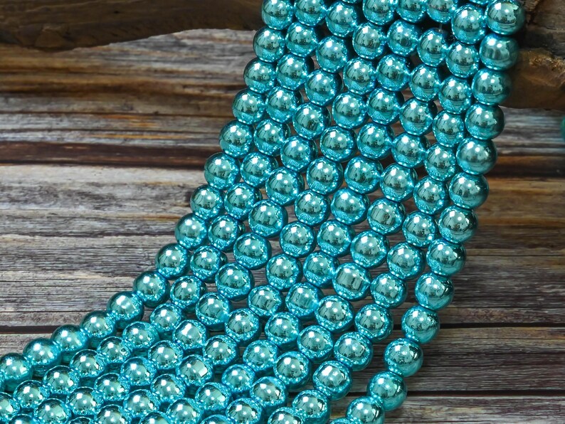 May include: A strand of turquoise blue glass beads with a metallic sheen. The beads are round and smooth, and they are arranged in a cascading pattern.
