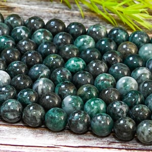 May include: A close-up of a strand of dark green and black jade beads. The beads are round and smooth, and they have a mottled appearance.