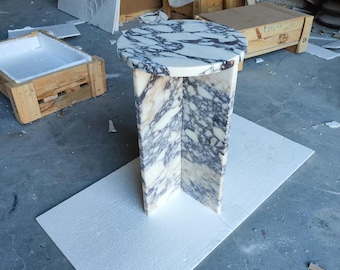 May include: A white and purple marble side table with a round top and a square base. The table is sitting on a white foam pad.