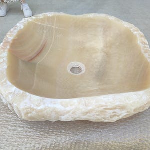 May include: A large, natural stone sink with a rough, textured exterior and a smooth, white interior. The sink has a round drain hole in the center.