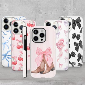 Può includere: Cinque custodie per telefono diverse con vari design. La prima custodia ha un motivo a fiocco blu e bianco. La seconda custodia ha un motivo a ciliegia rosa e bianco. La terza custodia ha un fiocco rosa e stivali da cowboy su uno sfondo a righe rosa e bianco. La quarta custodia ha un motivo a fiocco rosa e viola. La quinta custodia ha un motivo a fiocco nero e bianco.