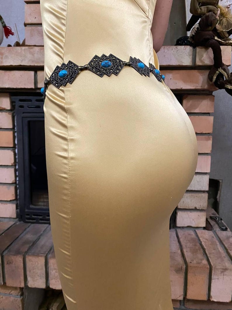 May include: A gold satin dress with a silver and turquoise belt. The belt has a geometric design with turquoise stones.
