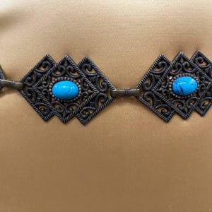 May include: A turquoise and silver filigree belt with a decorative design. The belt is made of metal and has a chain-like construction.