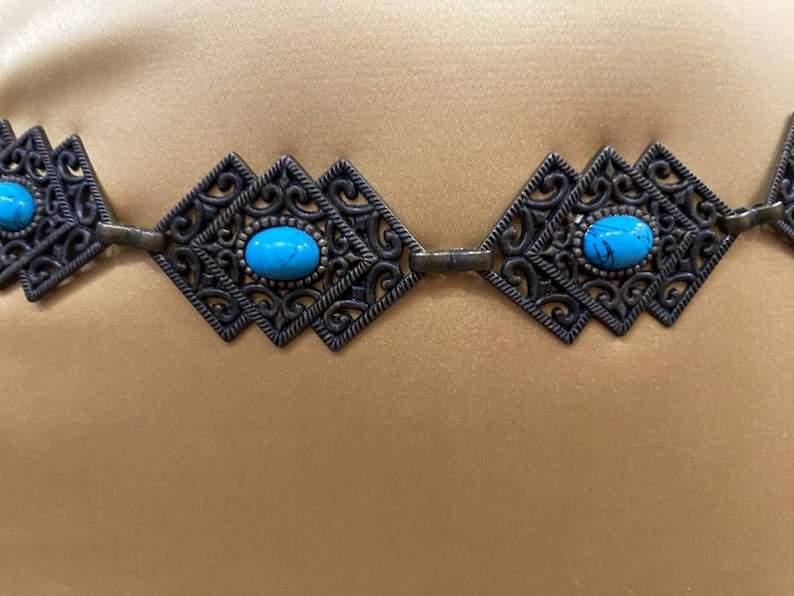 May include: A turquoise and silver filigree belt with a decorative design. The belt is made of metal and has a chain-like construction.