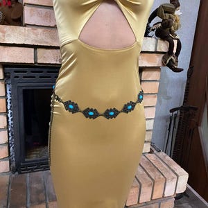 May include: A gold satin dress with a cut-out design and a turquoise and black beaded belt.