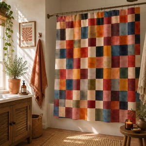 May include: A vibrant shower curtain featuring a patchwork pattern in various colours, including red, orange, blue, and beige. The curtain is suspended from a bronze rail in a bathroom, with a wooden cabinet and framed artwork.