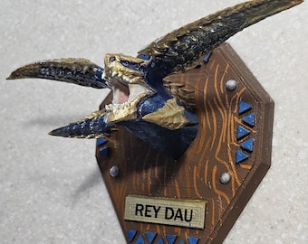 May include: A detailed, 3D-printed wall mount featuring a stylized dragon head with open mouth and sharp teeth. The dragon is painted in blue, gold, and brown tones, mounted on a wooden plaque with the text "REY DAU".