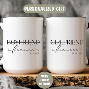 May include: Two white ceramic mugs with black handles and rims. One mug reads "BOYFRIEND fiance 01.23.2025", the other reads "GIRLFRIEND fiancée 01.23.2025". The mugs are on a wooden surface, with text that says "PERSONALIZED GIFT".