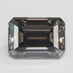 Op de afbeelding: Een grote, smaragdgeslepen edelsteen met een donkergrijze tint. De facetten van de steen reflecteren licht, waardoor een sprankelend effect ontstaat. De edelsteen staat tegen een effen witte achtergrond.