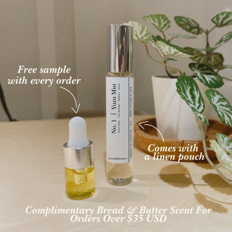 May include: A clear glass bottle labelled "No. 1 Yuzu Mist" with a silver cap and a smaller bottle with a dropper. The image includes the text "Free sample with every order" and "Comes with a linen pouch". A plant is in the background.