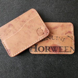 May include: Two light brown leather cardholders with white stitching. One cardholder has a horse logo and the other has the text "GENUINE HORWEEN". The leather has a distressed look.