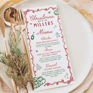 May include: A Christmas menu card with a festive design. The card features red and green illustrations and text, including "Christmas with the Millers" and a menu with starter, main, and dessert options. Gold cutlery and greenery are on the plate.