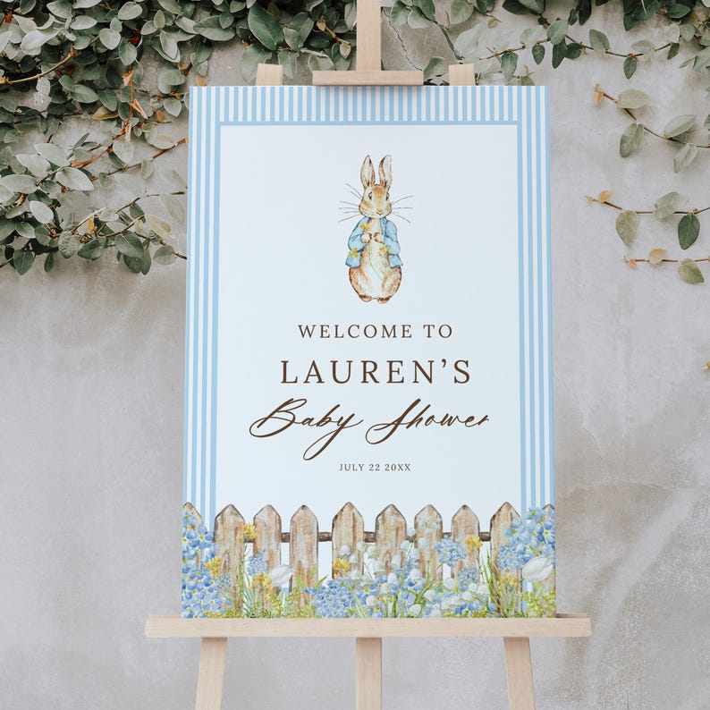 May include: A baby shower sign featuring a watercolor illustration of a rabbit wearing a blue jacket. The sign reads "Welcome to Lauren's Baby Shower" with a floral and picket fence border. The date is July 22, 20XX.