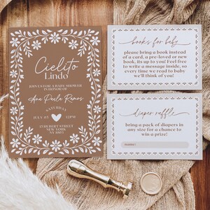 May include: A baby shower invitation suite featuring a brown and white floral design. The invitation includes the text "Cielito Lindo" and event details. Accompanying cards request books for the baby and a diaper raffle. A gold wax seal and stamp are also present.