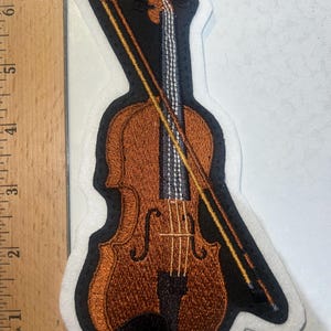 May include: A brown embroidered violin with a black bow and strings. The violin is on a white background.